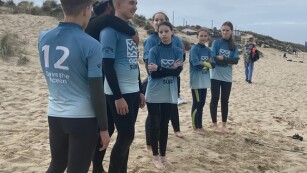 uczniowie w sportowych niebieskich koszulkach stoją na plaży