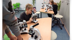 uczeń siedzi przy stoliki i korzysta z mikroskopu