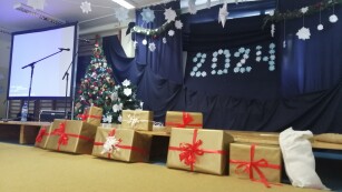 Sala na której znajduje się napis 2024, duże pudła zapakowane jak prezenty, tablica, mikrofony