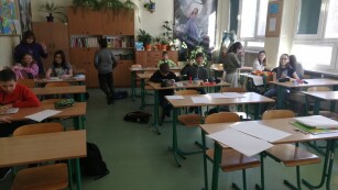 Uczniowie siedzą przy stolikach i wykonują zadania