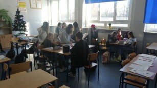 Uczniowie siedzą przy stolikach i wykonują zadania
