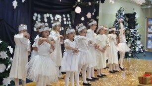 Dziewczynki ubrane w białe sukienki tańczą na scenie