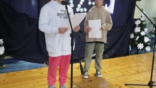 Dwie uczennice stoją na scenie, jedna z nich czyta tekst do mikrofonu