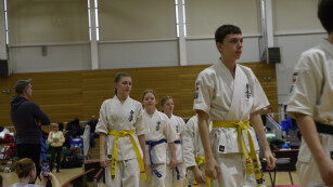 Uczniowie ubrani w białe kimona karate idą jeden za drugim