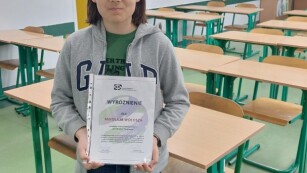 Uczeń w sali lekcyjnej prezentuje dyplom za wyróżnienie w konkursie