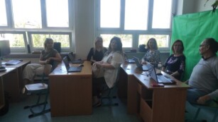 Nauczyciele siedzą przy biurkach z komputerami
